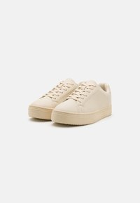 Sneaker in pelle beige con lacci piatti, punta arrotondata e suola in gomma testurizzata. Design minimalista con dettagli di cucitura sottili.