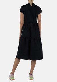 Abito nero al ginocchio con maniche corte, design a strati e tessuto morbido. Indossato con sneakers colorate con un logo sul tallone.