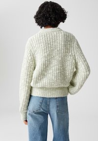 Maglione lavorato a maglia verde chiaro con un fit morbido, texture a coste, maniche ampie e un elastico in vita, abbinato a jeans blu a vita alta.