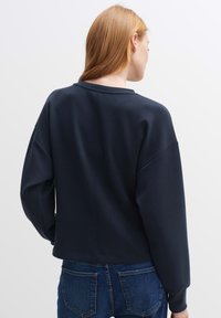 Felpa blu navy con spalle scese, scollatura rotonda e tessuto morbido. Caratterizzata da una lunghezza cropped e un design minimalista.