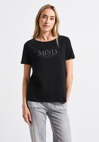 T-shirt en coton noir avec un col rond et des manches courtes. Présente un design imprimé avec le texte "FAITES DE VOTRE ESPRIT UN ENDROIT AGRÉABLE" en gris.