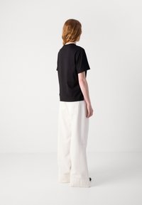 Svart t-skjorte med korte ermer kombinert med hvite, løstsittende bukser med brede ben og baklommer, sett fra bak. Minimalistisk design.