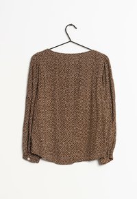 Blusa de lunares marrones hecha de tejido ligero. Presenta mangas largas, un cuello redondo y un detalle de botón en los puños.