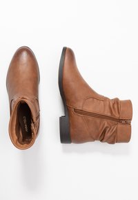 Bottes en cuir marron à la cheville avec un bout arrondi, fermeture éclair sur le côté et un dessus texturé. Talon bas et doublure intérieure lisse.
