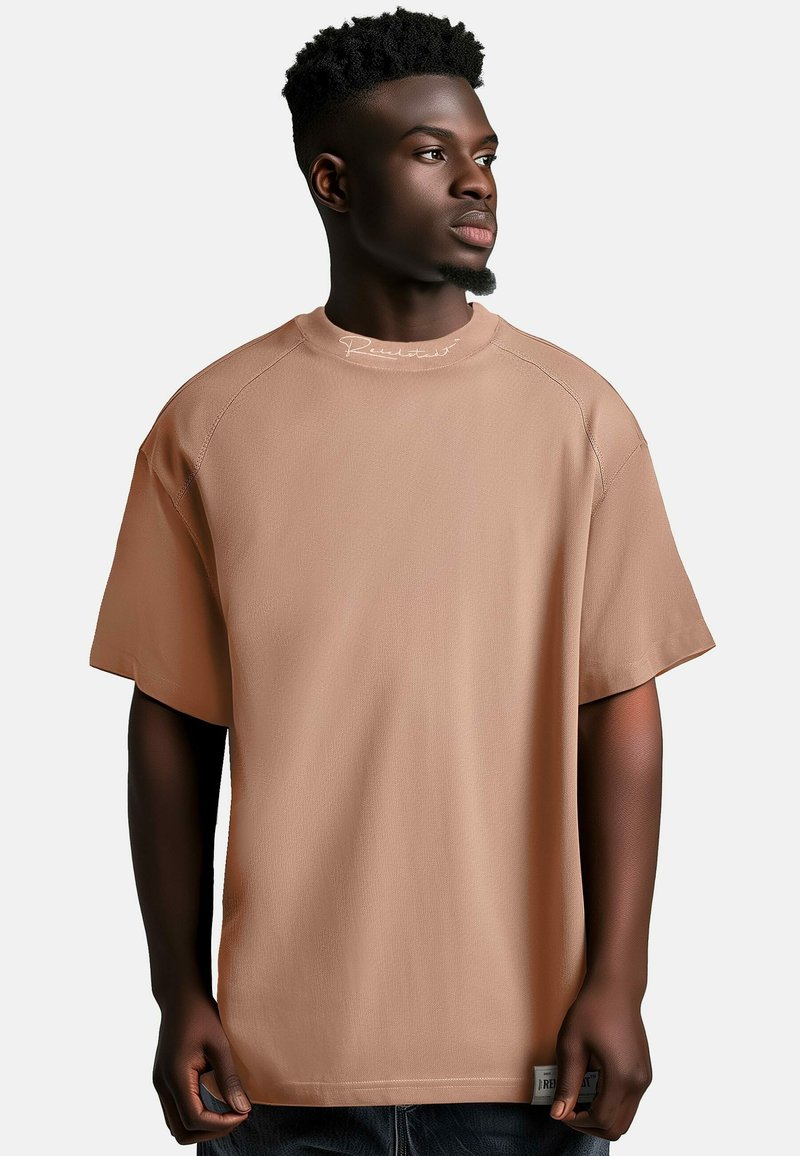 T-shirt oversize a maniche corte in beige chiaro, realizzato in tessuto morbido, con collo rotondo e dettagli di cucitura visibili sulle spalle.