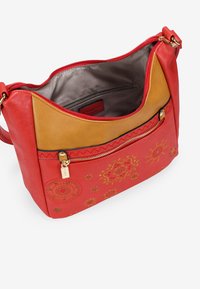 Bolso de mano de cuero rojo con un patrón floral dorado, una sección superior de cuero beige y un compartimento con cremallera. El interior cuenta con un forro suave.