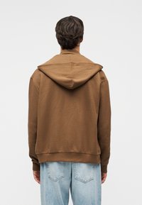 Καφέ φούτερ με υφή και φαρδιά κουκούλα με πλαίσιο. Διαθέτει ριμπ μανσέτες και τελείωμα, σε συνδυασμό με ανοιχτόχρωμο μπλε τζιν παντελόνι.