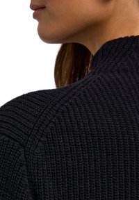 Maglione nero a maglia con texture a costine verticali, colletto alto e design delle spalle senza cuciture. Primo piano dei dettagli del tessuto.