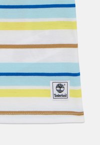 T-shirt en coton rayé avec des lignes bleu clair, jaune et marron. Dispose d'une étiquette logo Timberland cousue sur le côté inférieur droit.