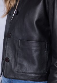 Black leather jacket featuring a smooth texture, round dark buttons, and a patch pocket on the left side. Tailored fit with a contemporary design.