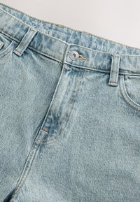 Slim-fit lichtblauwe spijkerbroek met rafelige randen, zilveren knoopsluiting en oranje stiksel details. Voorzien van een klassiek ontwerp met vijf zakken.