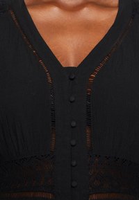 Abito nero con scollatura a V, chiusura a bottoni e dettagli in pizzo trasparente. Tessuto testurizzato con delicate aperture.