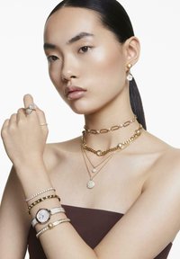 La joyería de oro incluye collares en capas, un choker con gemas y múltiples pulseras, que presentan diseños intrincados y texturas variadas.