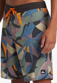 Men's swim shorts featuring a colorful, abstract leaf pattern in shades of green, blue, orange, and black with a black waistband and tie.