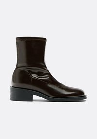 Bottine en cuir marron à profil fin, bout arrondi, accents cousus et petit talon bloc. Finition lisse avec texture brillante.