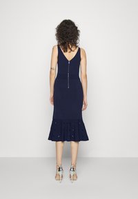 Robe ajustée bleu marine avec un ourlet flou, présente un dos en V et une fermeture éclair centrale. Fabriquée dans un tissu texturé avec des découpes.