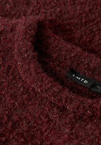 Bordeaux-farvet textured sweater med et loopet stofmønster. Har en tæt strikket krave og et mærke med teksten "LMTD."