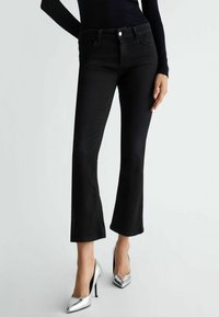 Jean en denim noir évasé avec taille mi-haute, dotés de poches avant et d'une fermeture à bouton, associés à des chaussures à talons hauts en argent brillant.