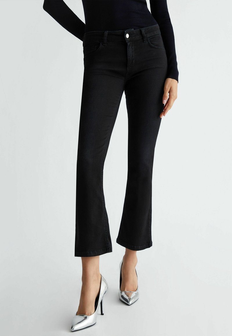 Jean en denim noir évasé avec taille mi-haute, dotés de poches avant et d'une fermeture à bouton, associés à des chaussures à talons hauts en argent brillant.