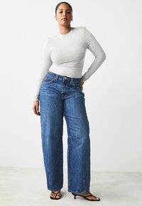 Top a maniche lunghe grigio chiaro abbinato a jeans in denim blu a gamba larga, con vita alta e una vestibilità rilassata, completato da sandali neri con tacco.