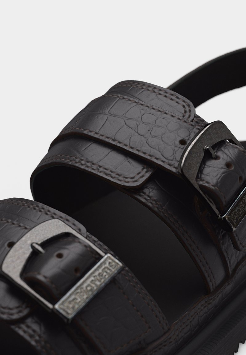 Close-up of dark brown textured leather sandal with two adjustable metal buckles and thick sole.