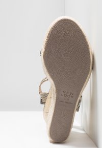 Sandale compensée beige clair avec une tige en liège texturé, une sangle ajustable et une semelle en caoutchouc grise. L'étiquette indique la taille et les informations d'origine.