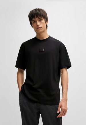 T-shirt noir à manches courtes en coton, avec un col rond et un petit logo rectangulaire sur la poitrine.