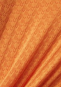 Ljust orange stickad tyg med ett texturerat mönster, som har zigzag-linjer och små punkterade designer överallt. Slät och flexibel.