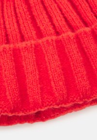 Tecido de malha vermelho com um padrão canelado, apresentando listras alternadas grossas e finas, textura suave e um acabamento ligeiramente peludo.