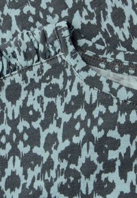 Bavlněná tkanina v světle modrém a tmavě šedém abstraktním leopardím vzoru s volánkovými detaily kolem výstřihu a šitými okraji.