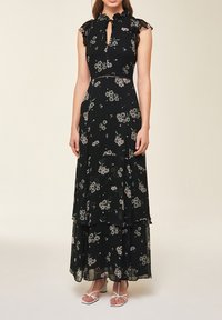 Svart blommig maxiklänning med volangärmar och nyckelhålsringning. Har ett lager av kjol och delikata blommönster i dämpade färger.