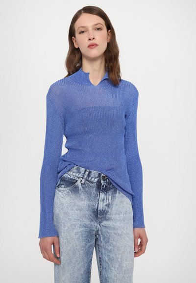 Blue ribbed long-sleeve shirt with a collar, paired with high-waisted light blue denim jeans. The shirt has a textured knit pattern.