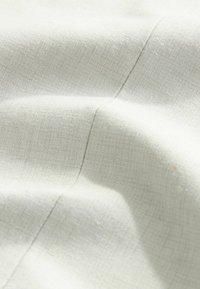 Gros plan d’un tissu en lin beige clair avec une texture de tissage visible et des ombres subtiles mettant en valeur les plis et les coutures.
