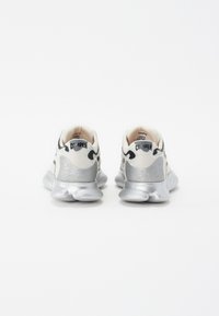 Sneakers with a white mesh upper, silver accents, textured heel, and a rounded, cushioned sole. Branding visible on the heel tab.