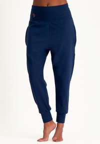 Dunkelblaue Jogginghose mit hohem, elastischem Bund, mäßig zulaufenden Beinen, seitlichen Taschen und orangefarbenem Logodetail am Bund.
