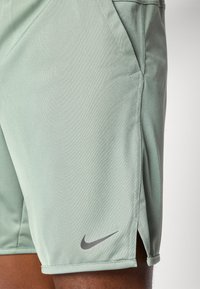 Pantalones cortos Nike de color verde claro con una tela texturizada, que presentan un logotipo de Nike en gris y cortes laterales para mayor movilidad.