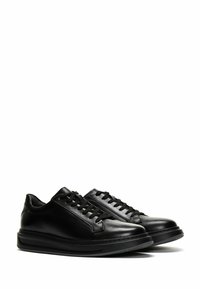 Baskets en cuir noir avec un embout arrondi, des lacets noirs plats et une semelle en caoutchouc noir texturé avec un subtil détail de design sur le côté.
