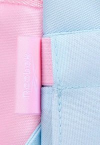 Primer plano de una tela texturizada rosa y azul con una etiqueta rosa de Reebok cosida entre los colores.