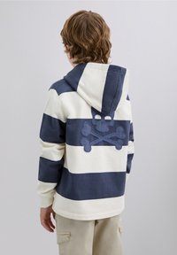 Sudadera con capucha que presenta franjas alternas en azul marino y crema. La parte posterior muestra un diseño bordado de calavera y huesos cruzados.