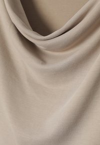 Tessuto beige drappeggiato con una finitura testurizzata, caratterizzato da morbide pieghe e un aspetto liscio, adatto per abbigliamento o accessori per la casa.