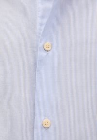 Primer plano de una tela de camisa a cuadros azul claro, con un cierre de botón que presenta un botón redondo de color claro en medio de una textura suave.
