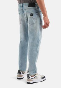 Jeans in denim azzurro chiaro con una vestibilità rilassata, dotati di tasche posteriori e un'etichetta nera. Abbinati a sneaker bianche e nere.