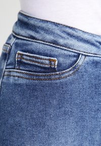 Ljusblå denimjeans har en detaljerad bakficka med kontrasterande sömmar, slät textur och en kurvad midjebandsdesign.