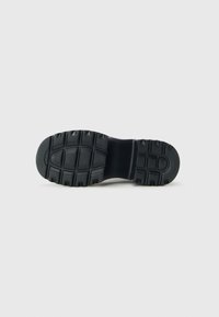 Black shoe sole with deep tread patterns designed for outdoor traction, displayed against a plain white background.
