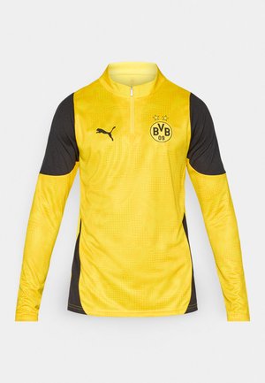 Langärmeliges Sportoberteil mit Viertelreißverschluss, hauptsächlich gelb mit schwarzen Akzenten an den Ärmeln, aus strukturiertem Stoff und mit einem Teamlogo.