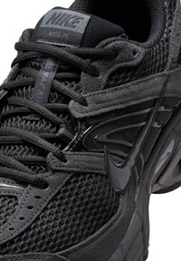 Κοντινή λήψη ενός μαύρου sneaker Nike Moto 2K που δείχνει πλεκτό ύφασμα, επενδύσεις από σουέντ, κορδόνια και λογότυπο Nike στο πλάι και στη γλώσσα.