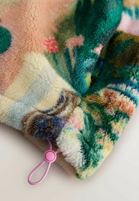 Pătură pufoasă, multicoloră, cu model floral. Prezintă o textură moale, margini rotunjite și un șnur roz în colț.