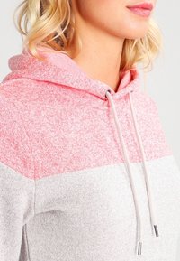 Capuchontrui met een kleurenblokdesign met een roze gemêleerd bovenste deel en een lichtgrijs onderste deel. Voorzien van trekkoorden en een zachte textuur.