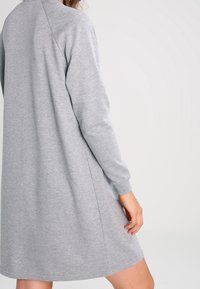 Grå sweatshirtklänning med långa ärmar, tillverkad av mjuk tyg. Har en avslappnad passform, rundad halsringning och knälång design.
