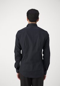 Maglietta nera a maniche lunghe con un design aderente, caratterizzata da un colletto standard, polsini con bottone e una texture di tessuto liscia.